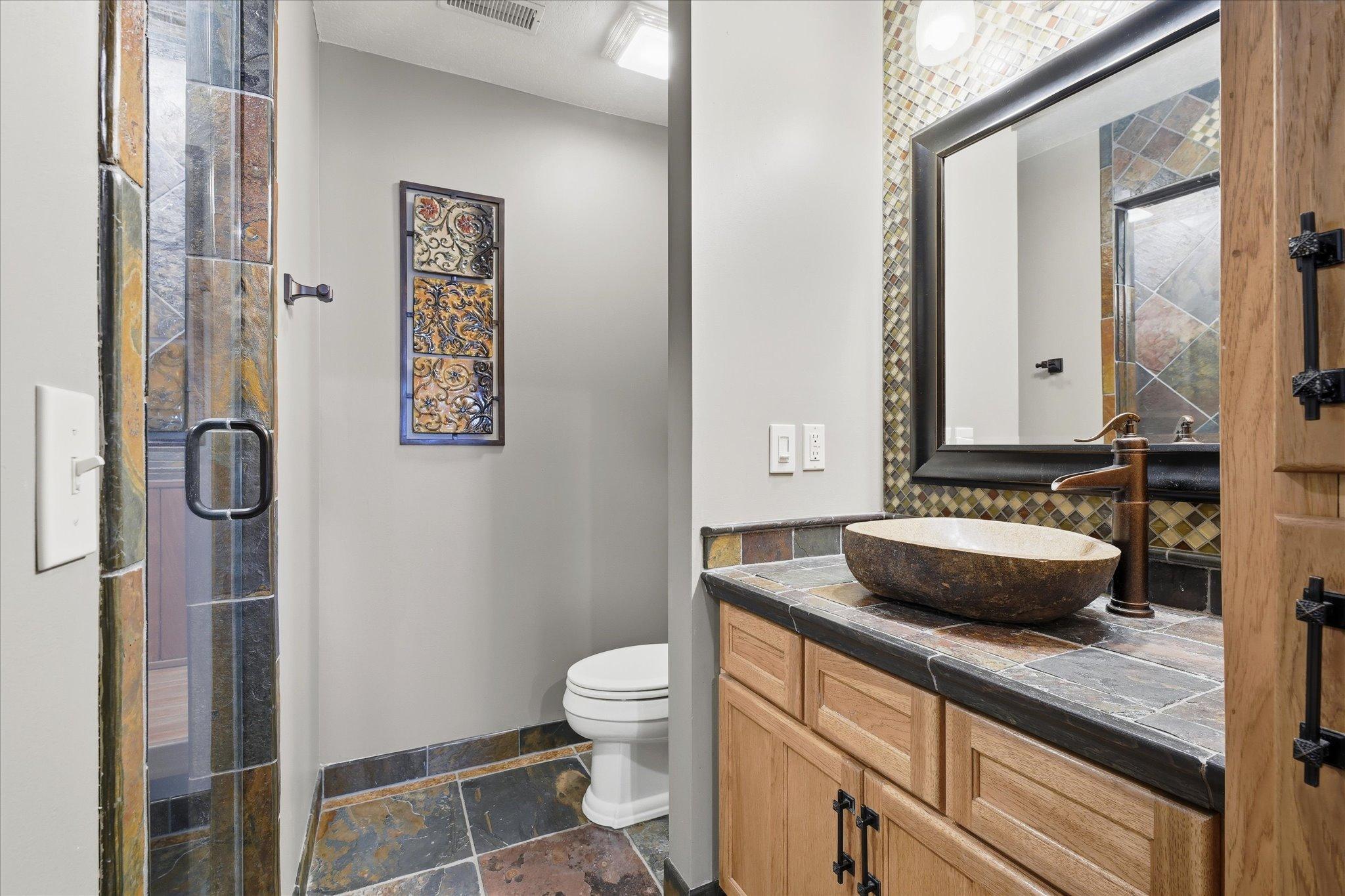 Lower-level 3/4 bathroom with heated floors, showcasing a stunning custom tile shower with bench seating, elegant stone vessel sink, and artisan-quality finishes that bring warmth and luxury to the space.