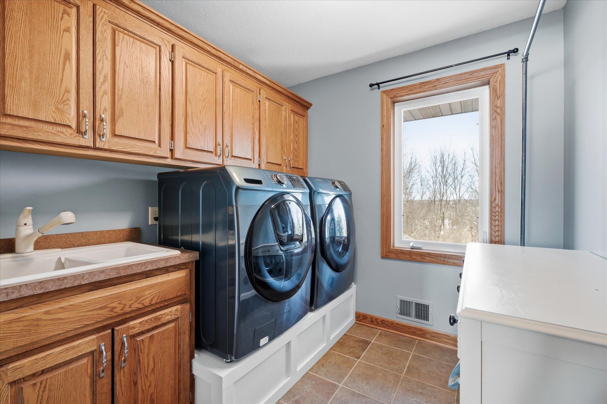 Upper-level laundry room equipped with cabinets for storage and a utility sink with sprayer, making laundry tasks easier and more efficient.