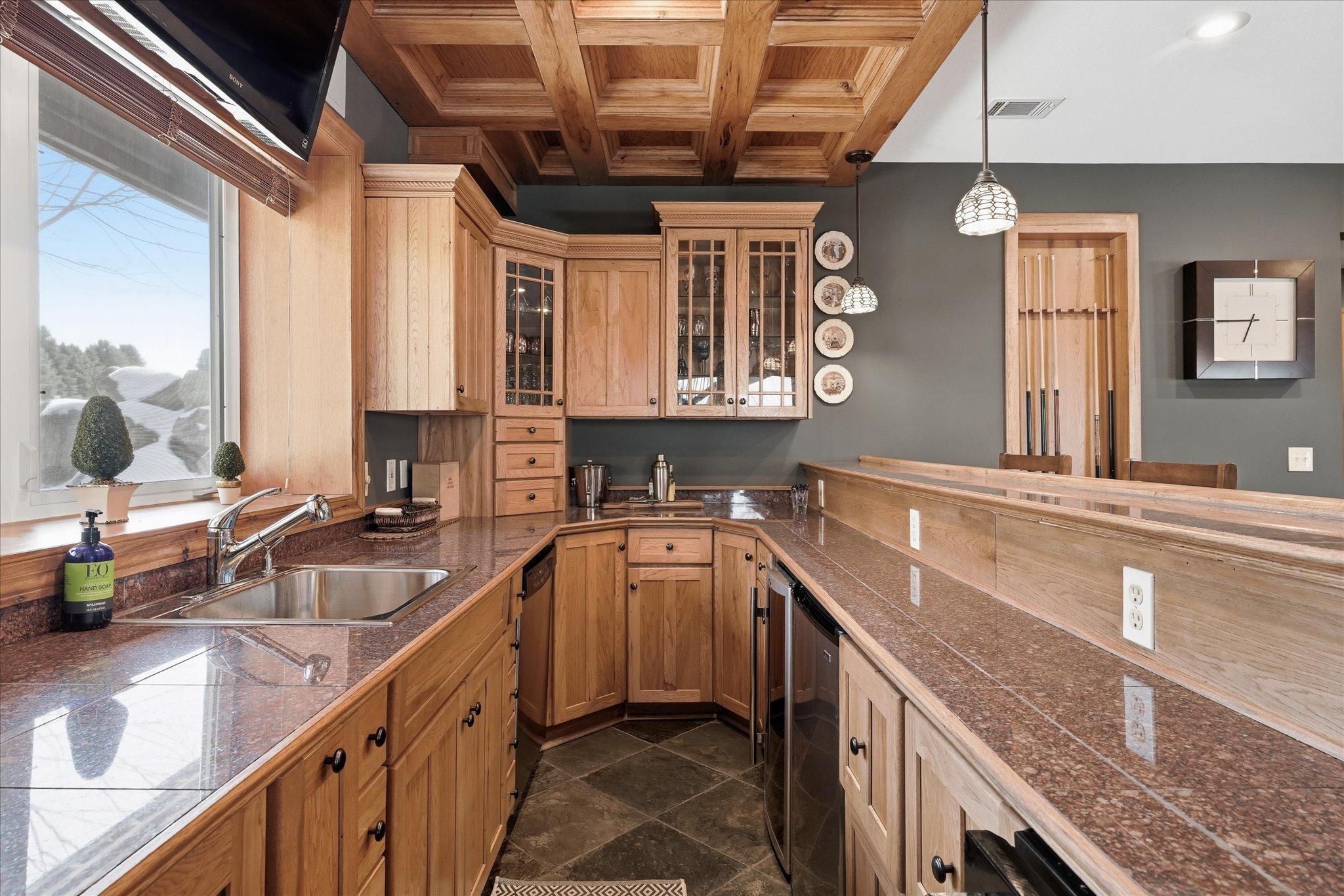 Featuring custom millwork, a striking coffered wood ceiling, granite surfaces, and a spacious wraparound bar with seating.