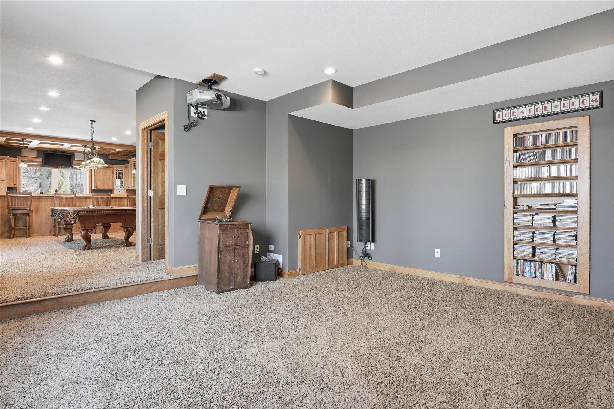 Lower-level media/theater room featuring a projector and built-in shelving, creating the perfect space for movie nights and entertainment. (Speakers are not included.)