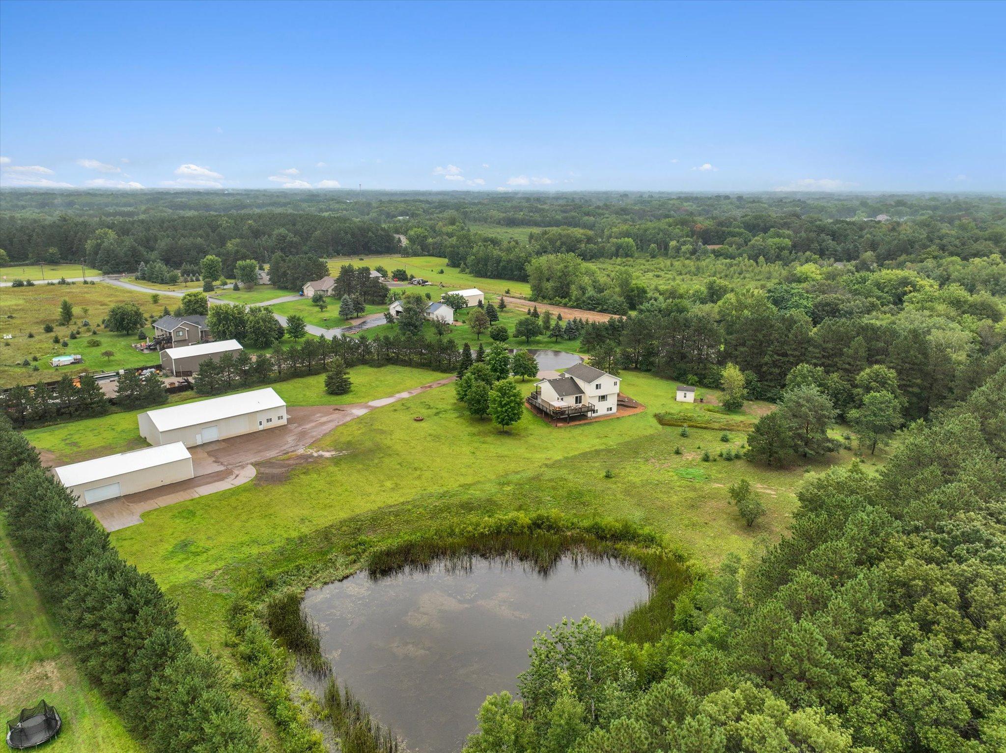 Full aerial overview captures the home, pond, acreage, and both outbuildings in one comprehensive view.