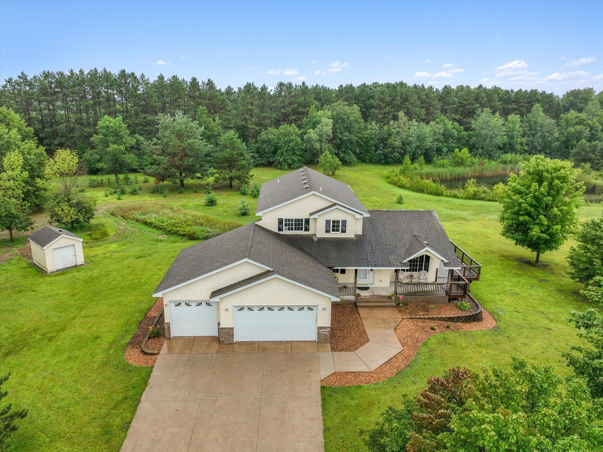 Aerial front view shows the home’s placement within the acreage, with mature tree coverage, open lawn, and a natural pond enhancing the setting.