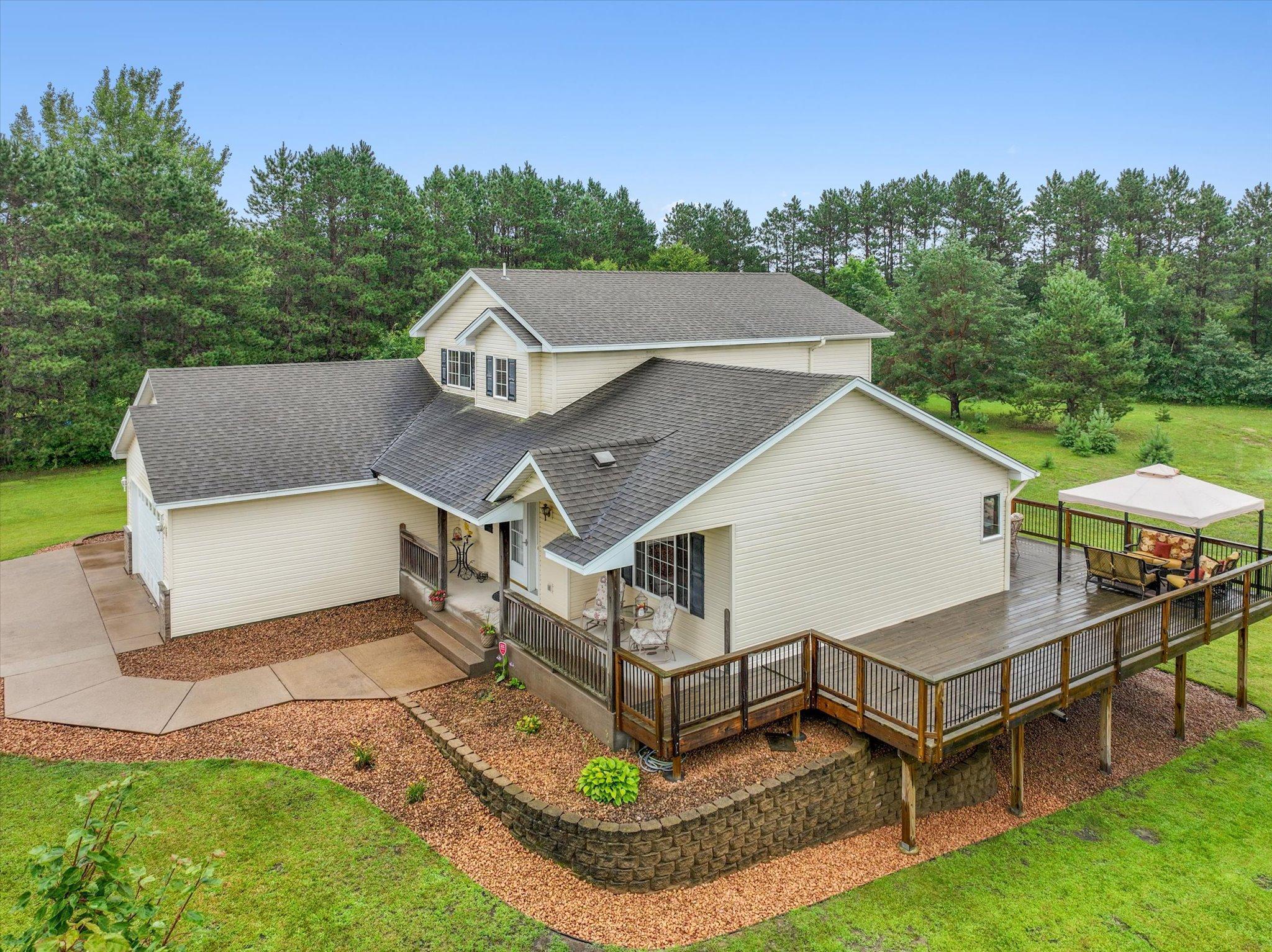 Elevated exterior view shows the home, deck, and landscaped approach from above.
