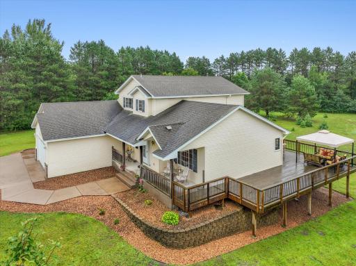 Elevated exterior view shows the home, deck, and landscaped approach from above.