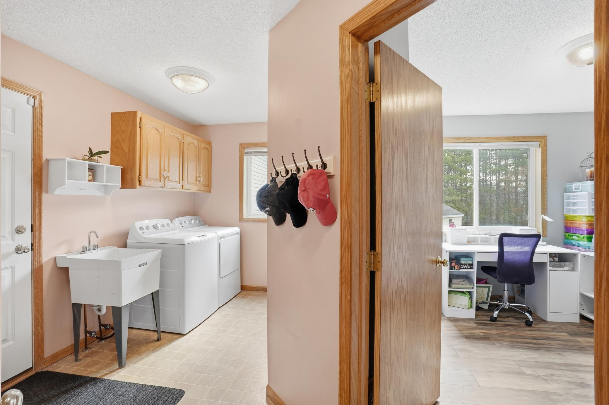 Functional main-level laundry/mudroom with utility sink, storage cabinetry, and adjacent flexible office/hobby room.