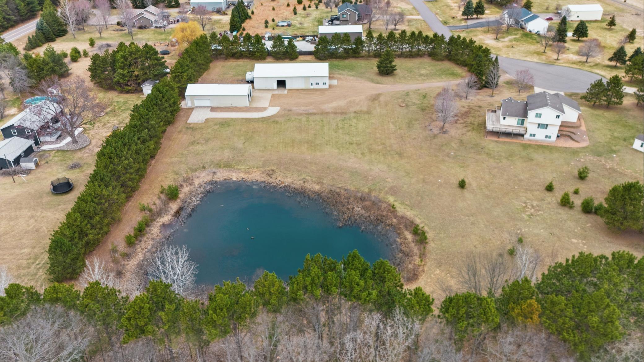 Elevated rear aerial showcases the scenic pond setting framed by mature trees and private acreage.