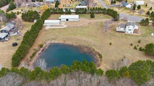 Elevated rear aerial showcases the scenic pond setting framed by mature trees and private acreage.