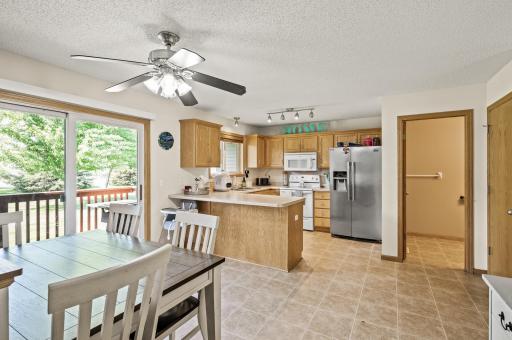 Open concept kitchen and dining area with breakfast bar seating, stainless steel refrigerator, abundant oak cabinetry, and walkout to private deck.