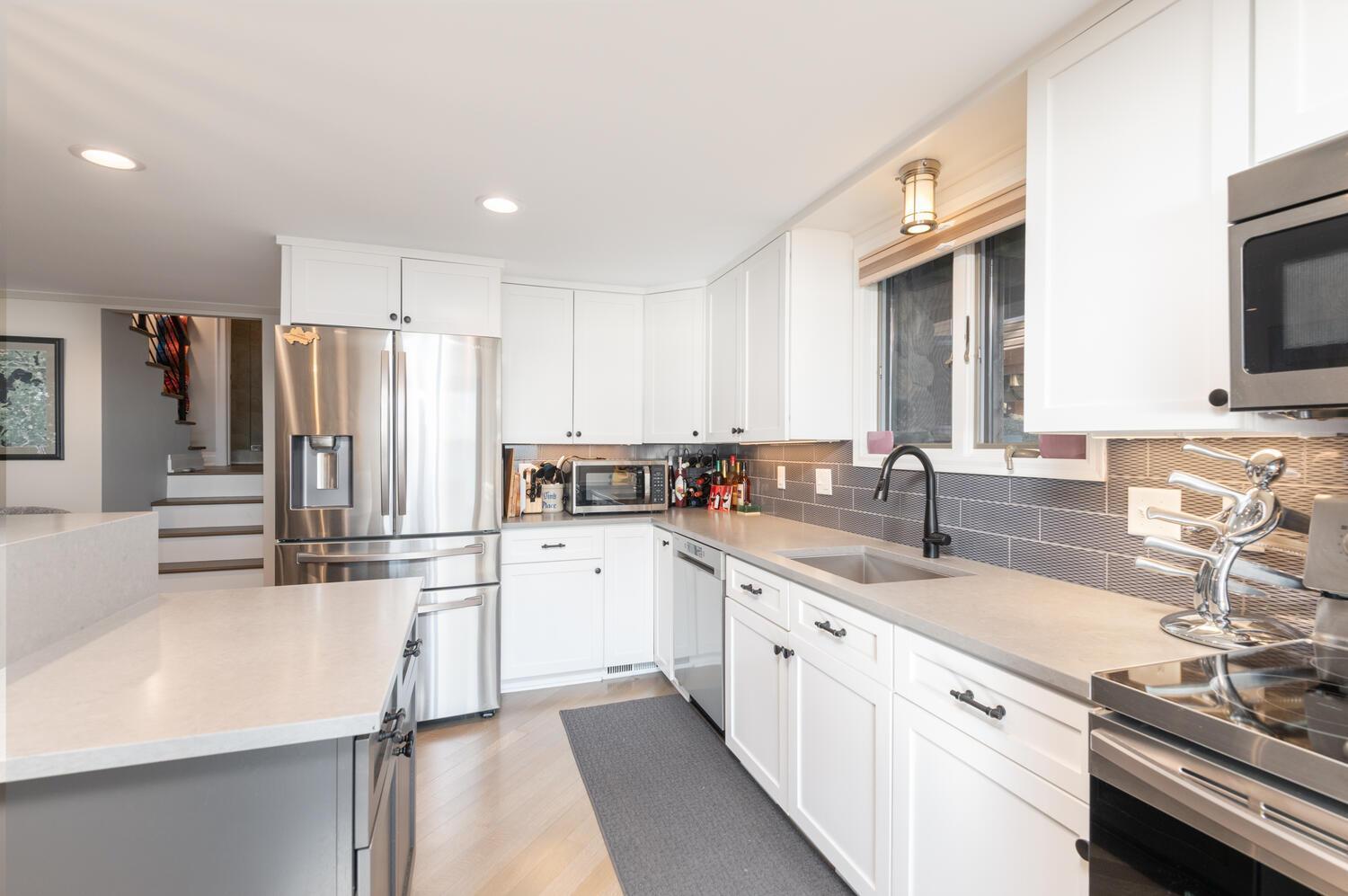 The bright remodeled kitchen includes enameled cabinetry, Corian counter tops, subway tile back splash and stainless appliances.