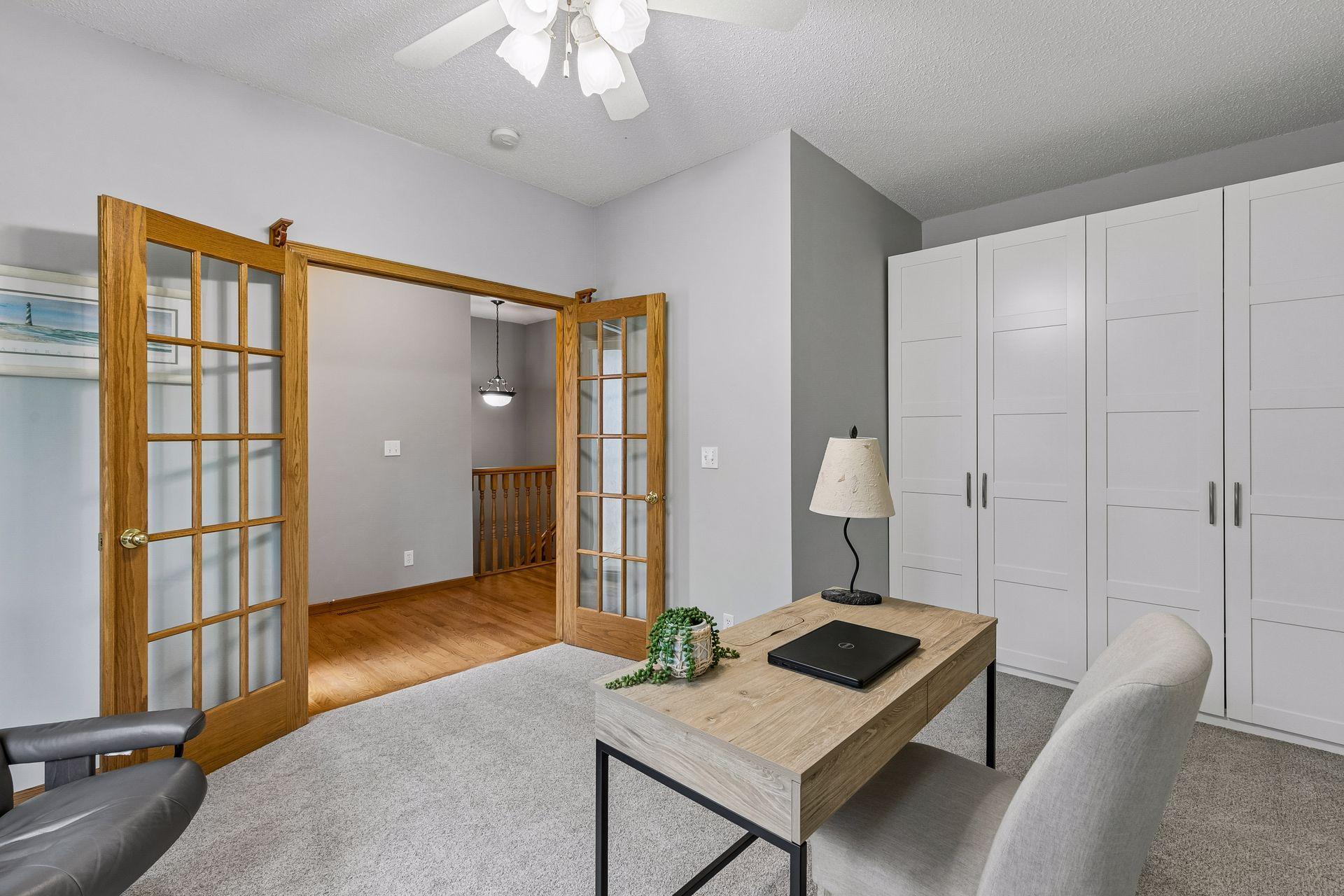 Bright main-level bedroom or office with French doors, custom storage, and front-facing windows. Perfect flexible-use space for remote work or guests.