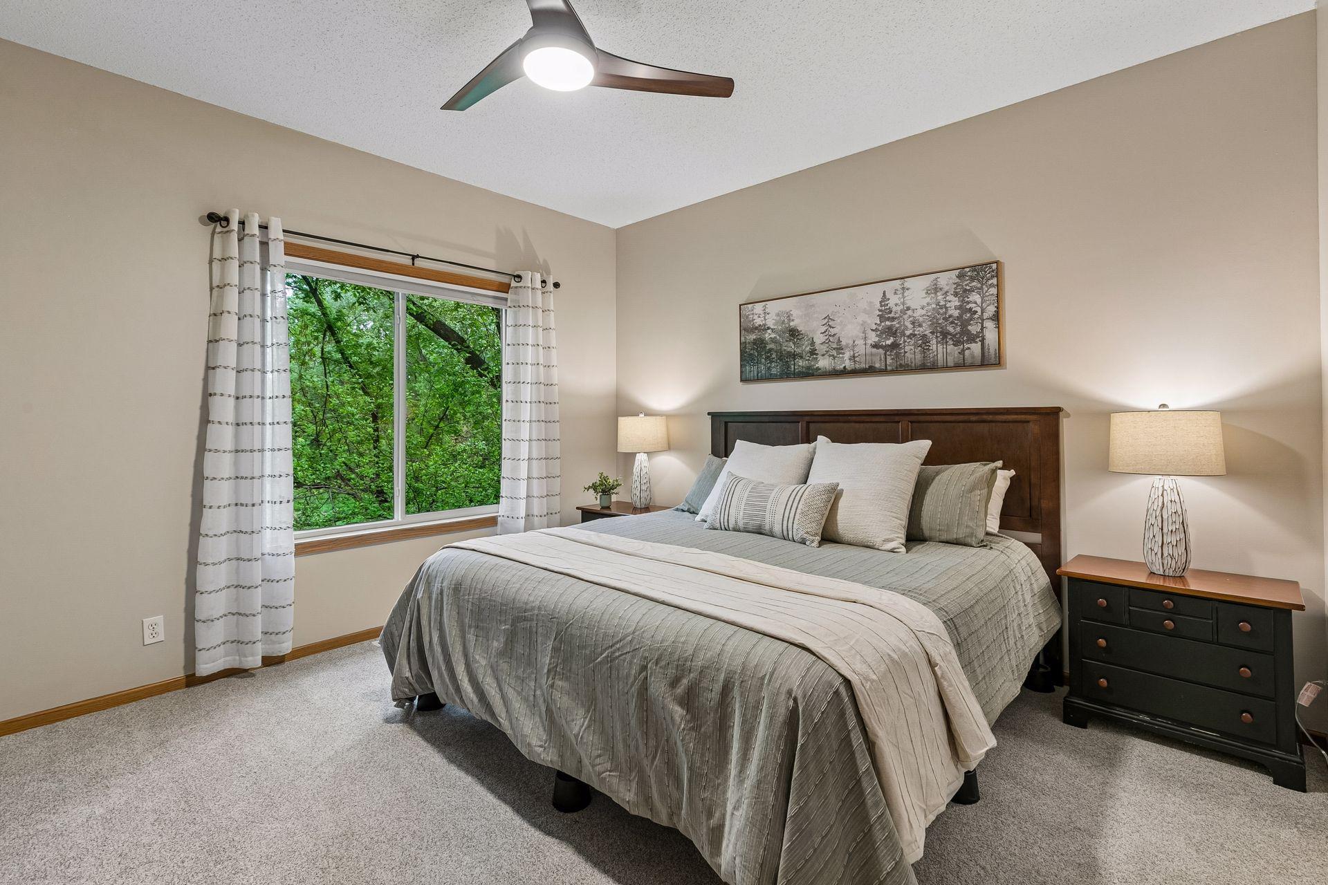 Spacious primary bedroom on the main level with large windows, peaceful tree views, neutral finishes, and generous layout for comfortable one-level living.