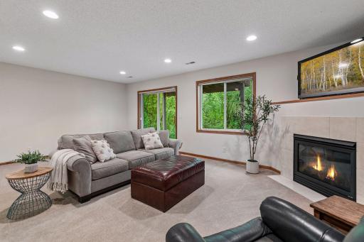 Cozy lower-level family room with gas fireplace, recessed lighting, soft carpet, and sliding door access to peaceful wooded views outside.