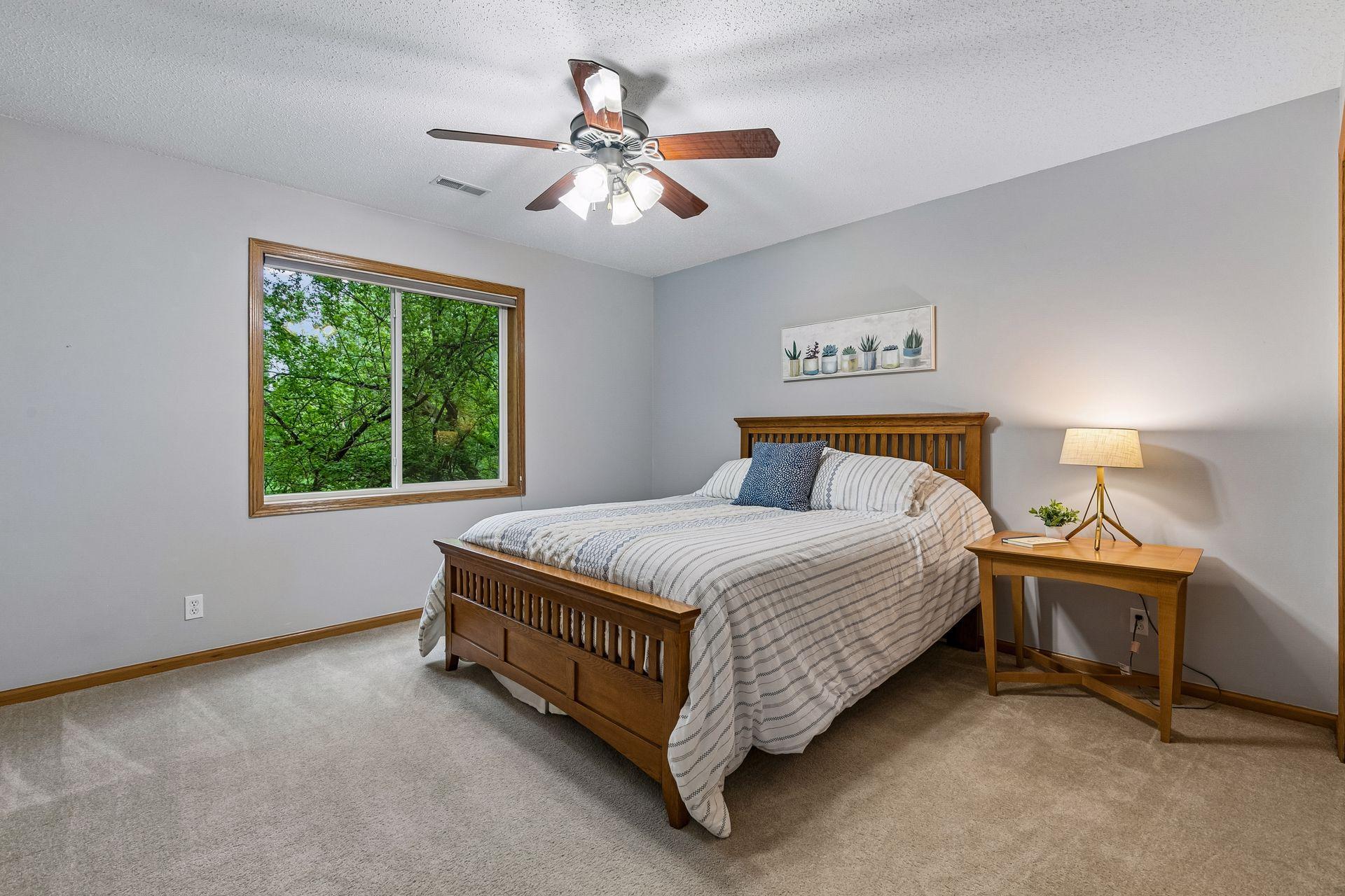 Comfortable third bedroom on the lower level with large window, soft carpet, and calming natural light overlooking mature trees.