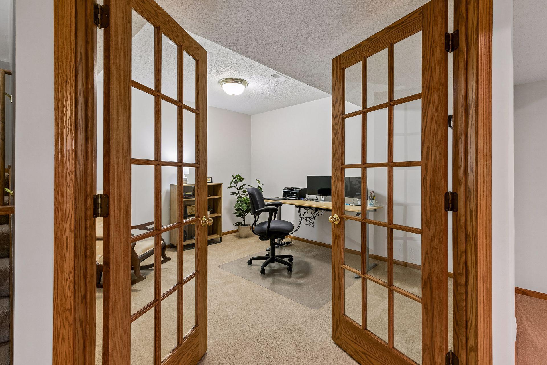 Private lower-level office or hobby room with elegant French doors, soft carpet, and flexible space ideal for working from home, crafts, or a quiet retreat.