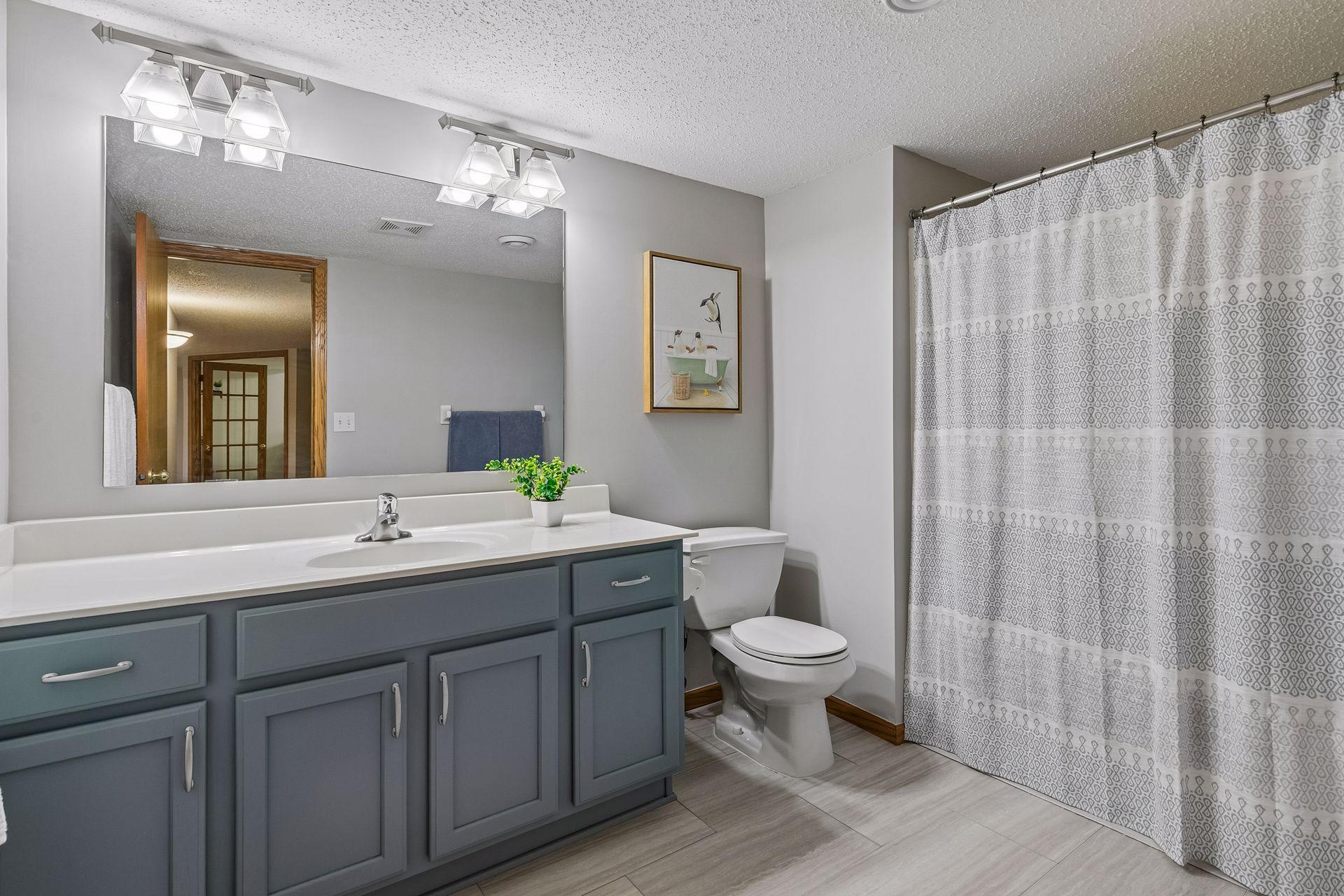Updated lower-level full bathroom with large vanity, modern lighting, tile flooring, and shower/tub combination.