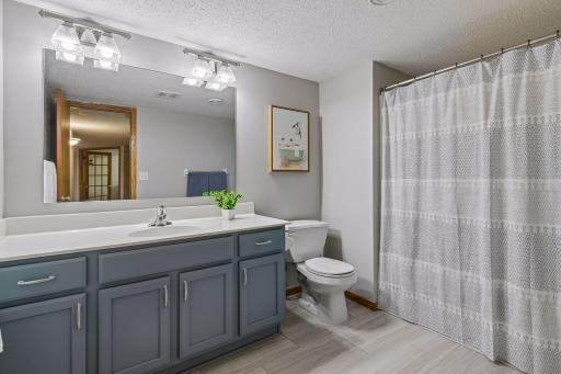 Updated lower-level full bathroom with large vanity, modern lighting, tile flooring, and shower/tub combination.