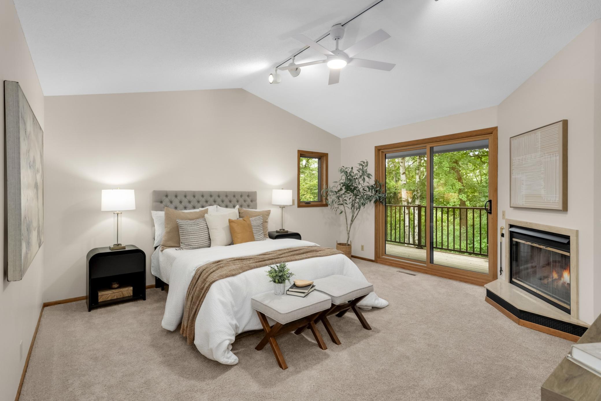 A private primary bedroom oasis featuring vaulted ceilings, a cozy fireplace and balcony access with peaceful wooded views.
