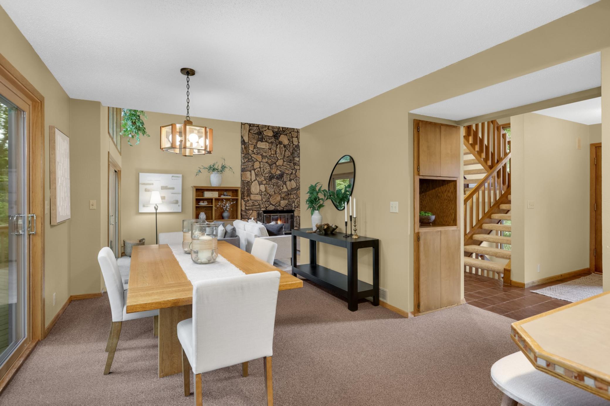 The open dining area overlooks the dramatic two-story great room, where a floor-to-ceiling stone fireplace creates a warm focal point and soaring windows bring the outdoors in.