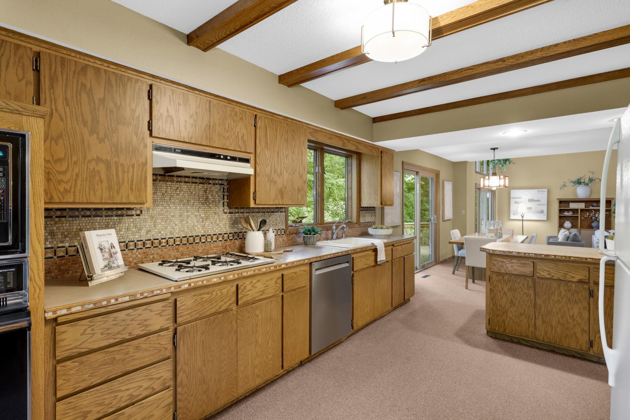 The spacious kitchen showcases warm wood cabinetry, a hand-laid tile backsplash, exposed ceiling beams and abundant storage and workspace.