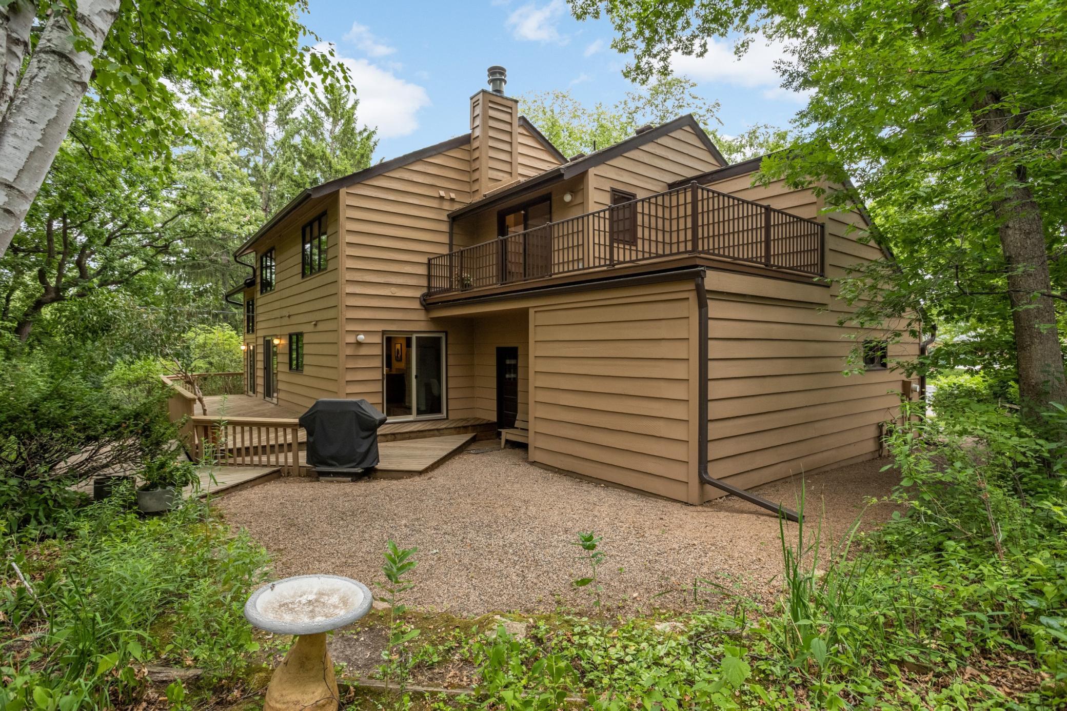 The private backyard is surrounded by mature trees and features multiple outdoor spaces, including a spacious deck, upper-level balcony and patio area.