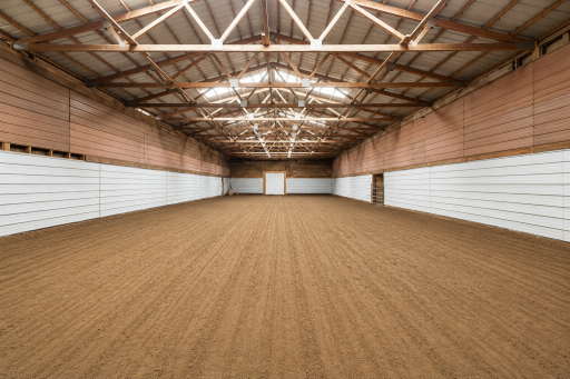 The expansive layout features a large open-span area with a sand footing, ideal for indoor riding, training, or equipment storage.