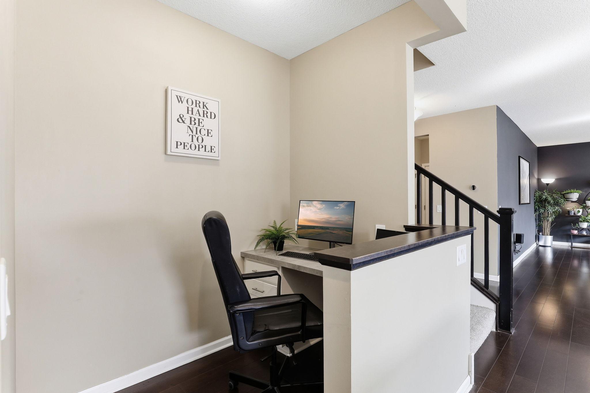 A built-in main-floor office nook sits adjacent to the kitchen, elevated above the living area with a sleek half-wall and black railing. Ethernet-wired and smartly integrated into the home's design.