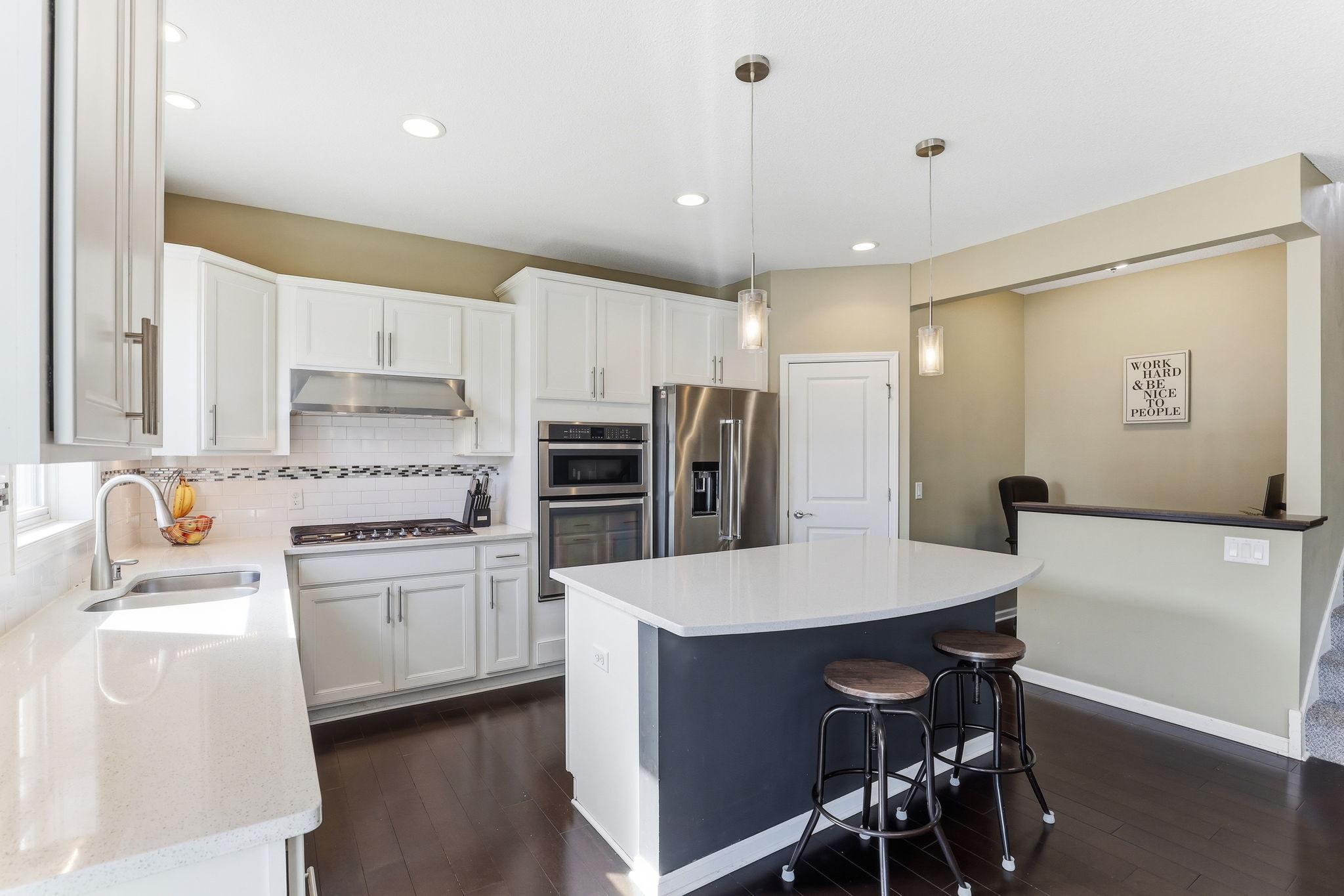 White cabinetry to the ceiling, quartz countertops, subway tile backsplash, gas cooktop, double wall oven, and a statement navy island with bar seating. Designed to perform at the highest level.