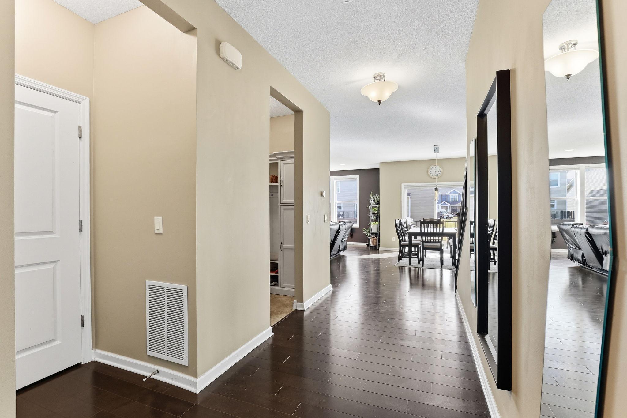 A generous main-level hallway runs on rich hardwood floors, connecting the entry, mud room, and main living area in one clean, uninterrupted sightline toward the bright dining and living zones.