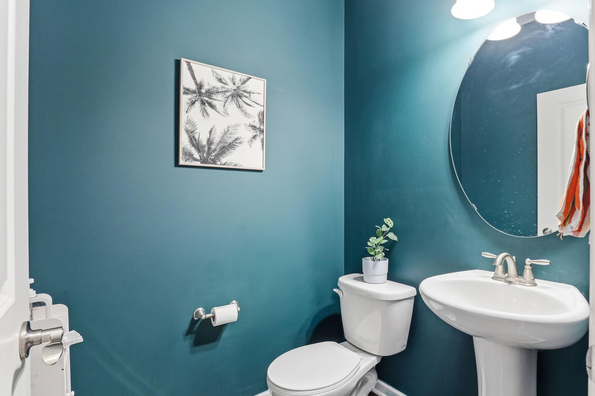 The main-floor powder room makes a statement with a bold teal accent wall, a pedestal sink, a round mirror, and brushed-nickel fixtures. Small in footprint, refined in execution