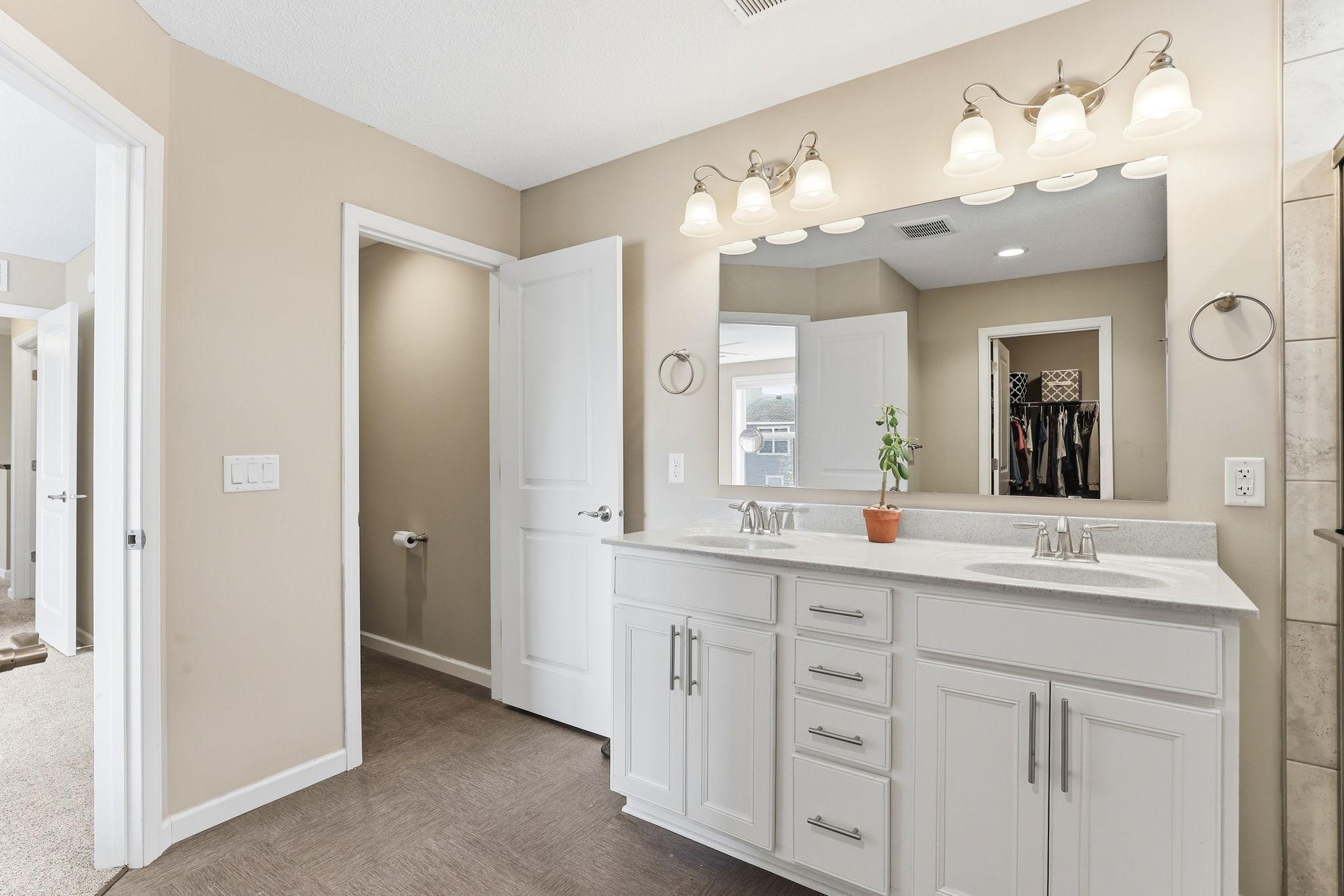 An expansive double vanity reflects in the full-width mirror, filling the primary bath with light. The walk-in closet sits just steps away through a private, dedicated door.