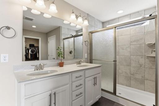 The 3/4 primary ensuite offers a double-sink vanity with quartz countertops, white cabinetry, brushed nickel fixtures, and a large tiled walk-in shower with a glass slider door.
