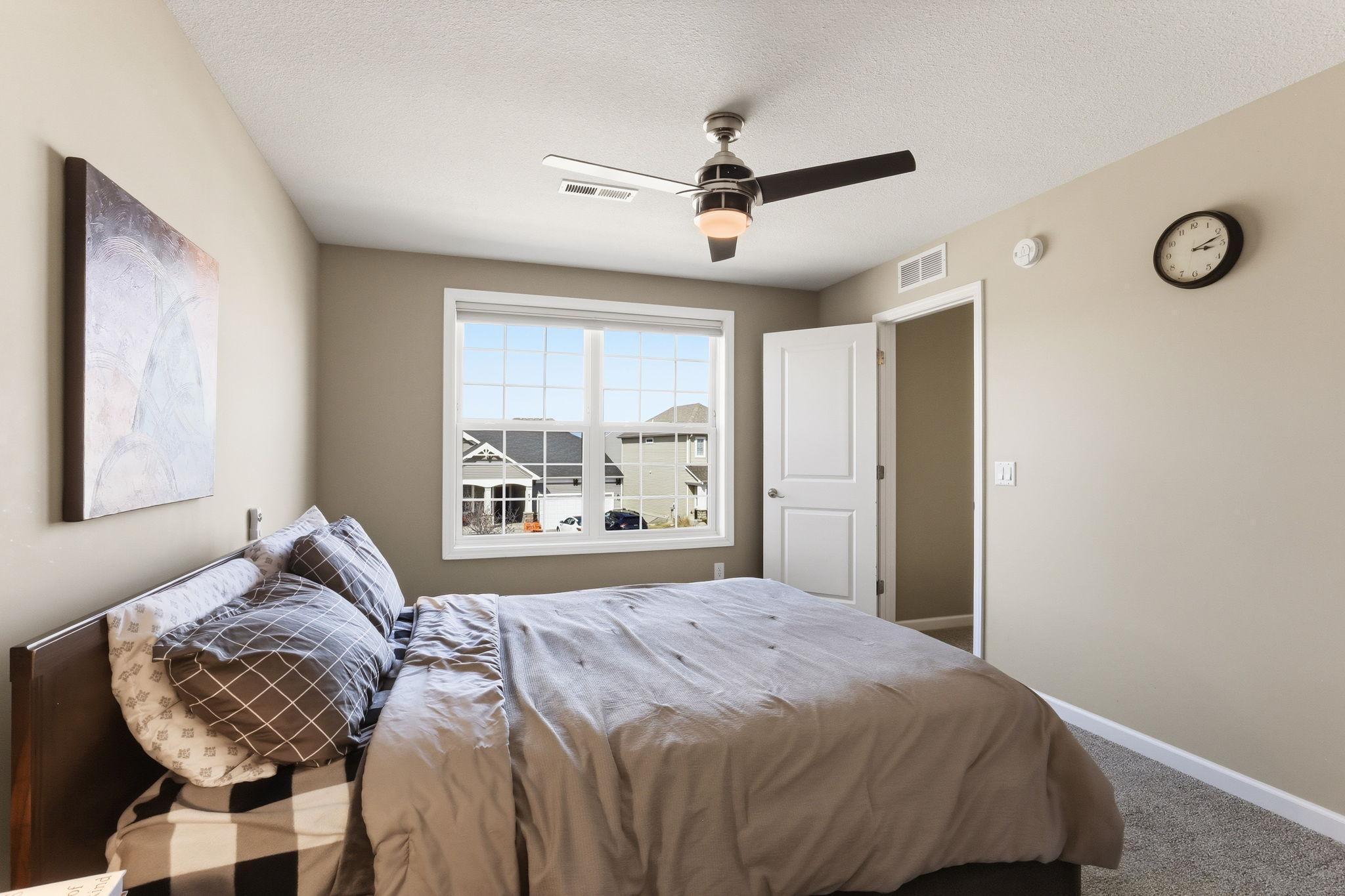 A serene, neutral fourth bedroom with plush carpet, a ceiling fan, and a bright window. The calm palette and generous proportions make it ideal as a guest room, nursery, or secondary home office.