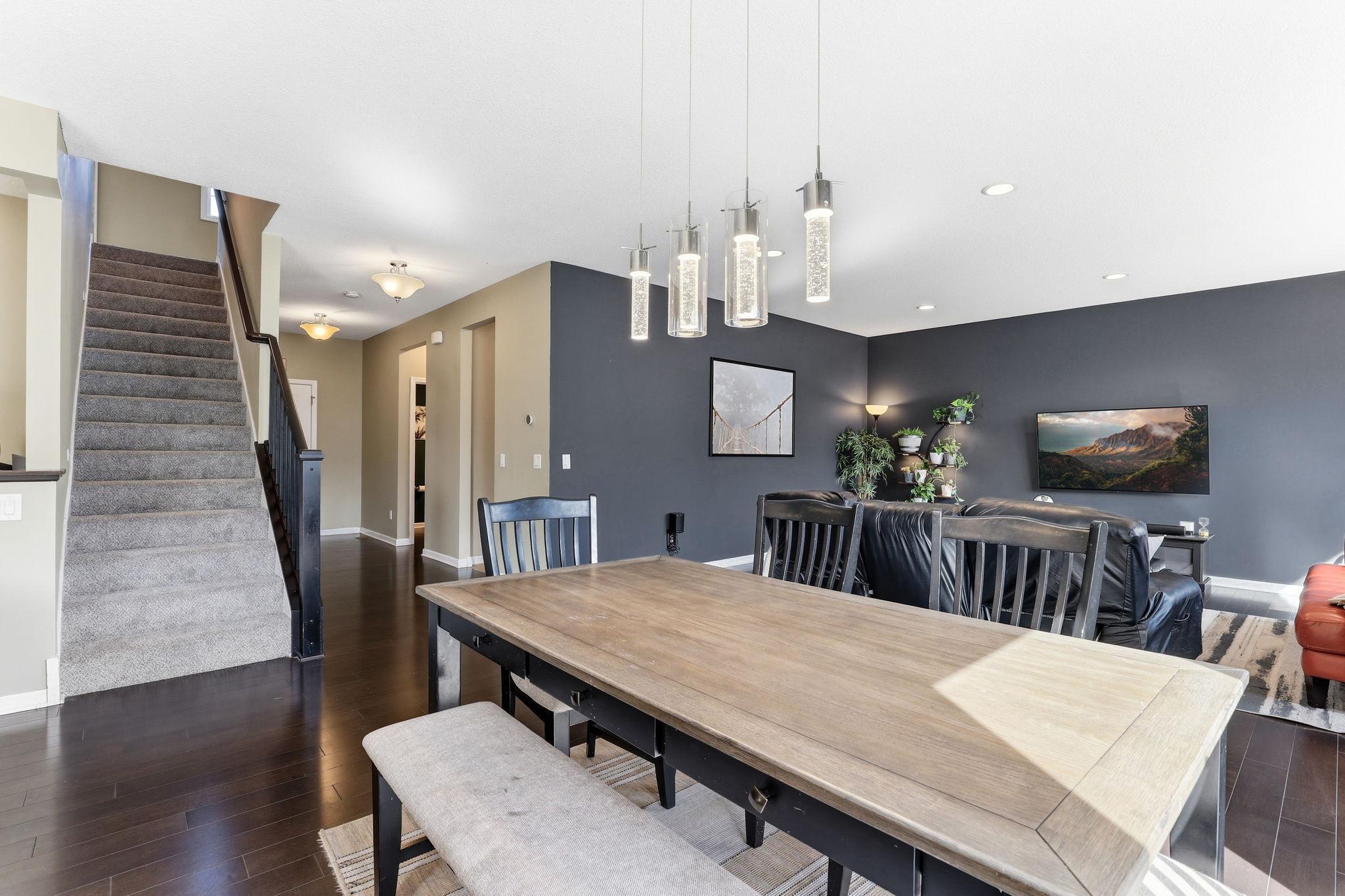 Sculptural glass cylinder pendants cast warm, intimate light over the dining space, adding a curated designer detail to this naturally bright and connected living and dining area.
