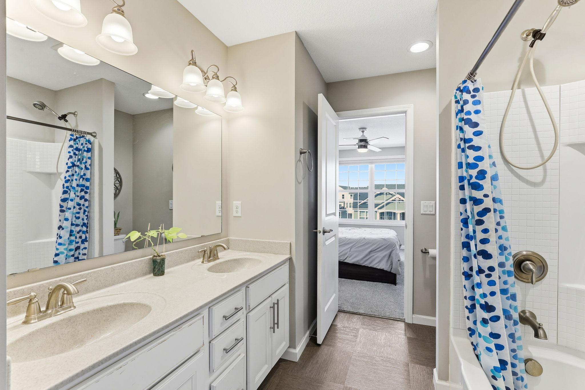 The full Jack-and-Jill bath serves two bedrooms with a double-sink vanity, quartz countertops, white cabinetry, and a tiled tub-shower combo. Thoughtfully designed for busy households.