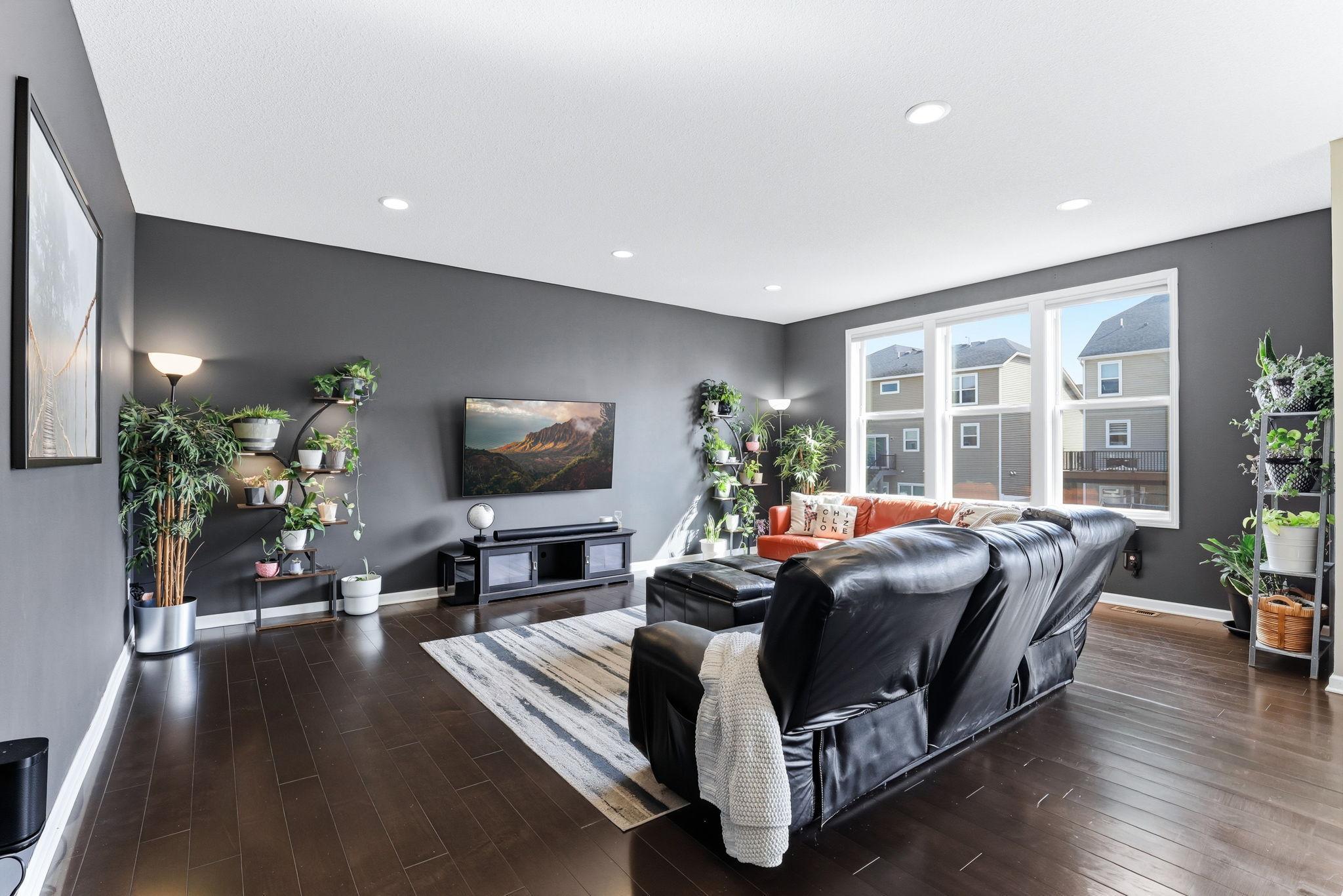 Bold charcoal accent walls and gleaming dark hardwood floors give this living room real presence. Recessed lighting, large windows, and an effortless scale make the space as functional as it is refined.