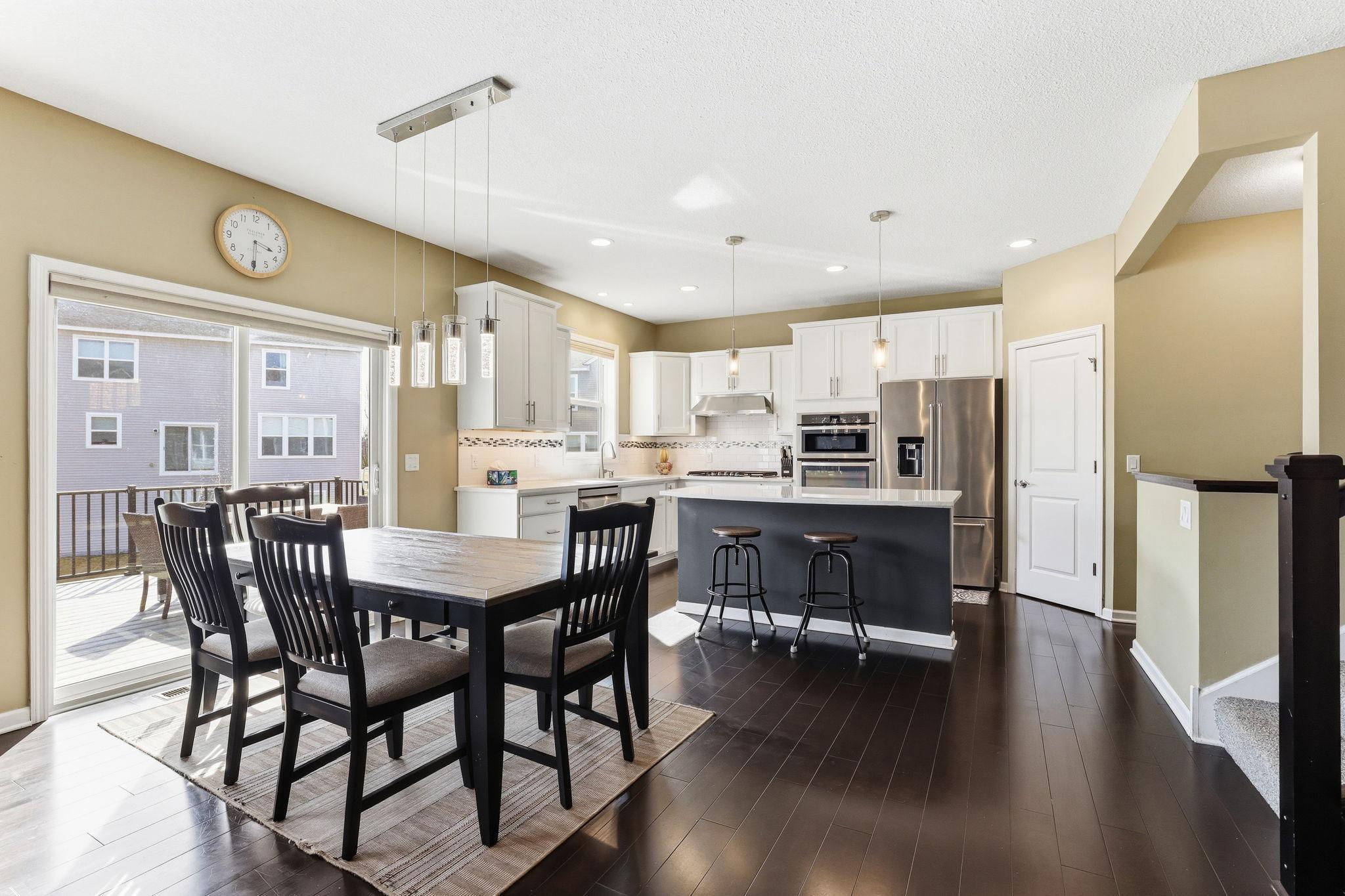 Sun pours through the slider to the composite deck, illuminating the dining area where statement pendant lighting and a clear sightline to the kitchen make everyday meals feel like an occasion.