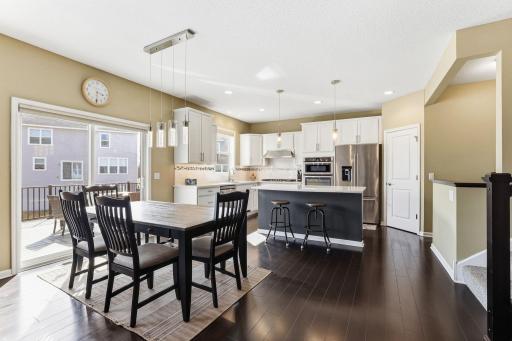Sun pours through the slider to the composite deck, illuminating the dining area where statement pendant lighting and a clear sightline to the kitchen make everyday meals feel like an occasion.