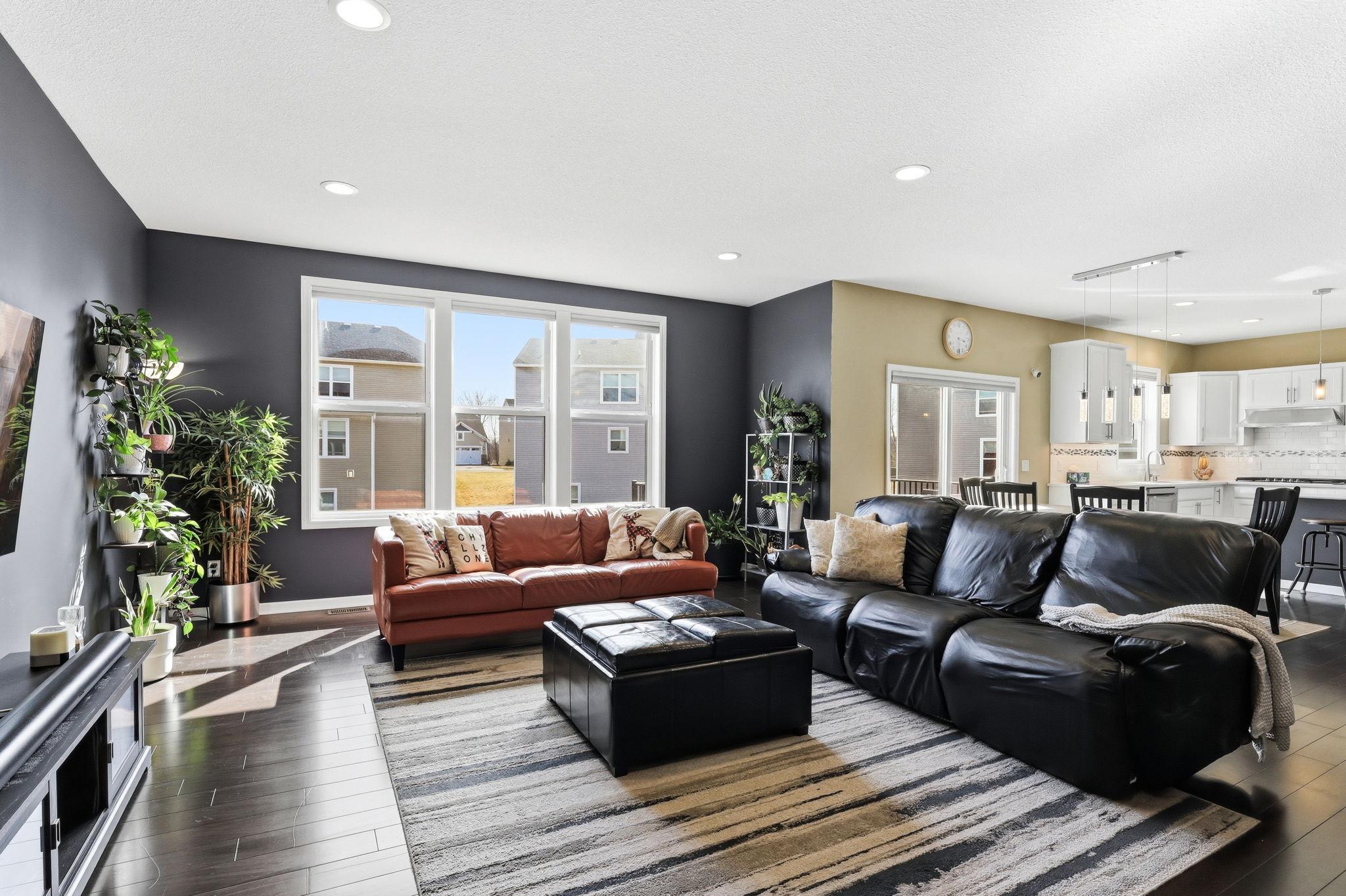 From the living area with a custom bump-out addition, the main level flows toward the kitchen and dining zone. Crisp white cabinetry and stainless steel appliances are visible just beyond, tying the entire floor together in one cohesive design.