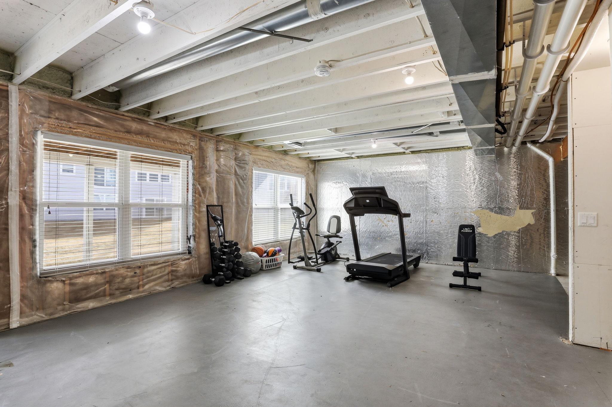 Dedicated gym space in the lower level with treadmill, elliptical, and free weights, plus natural light from ground-level windows. A compelling use of unfinished square footage today.