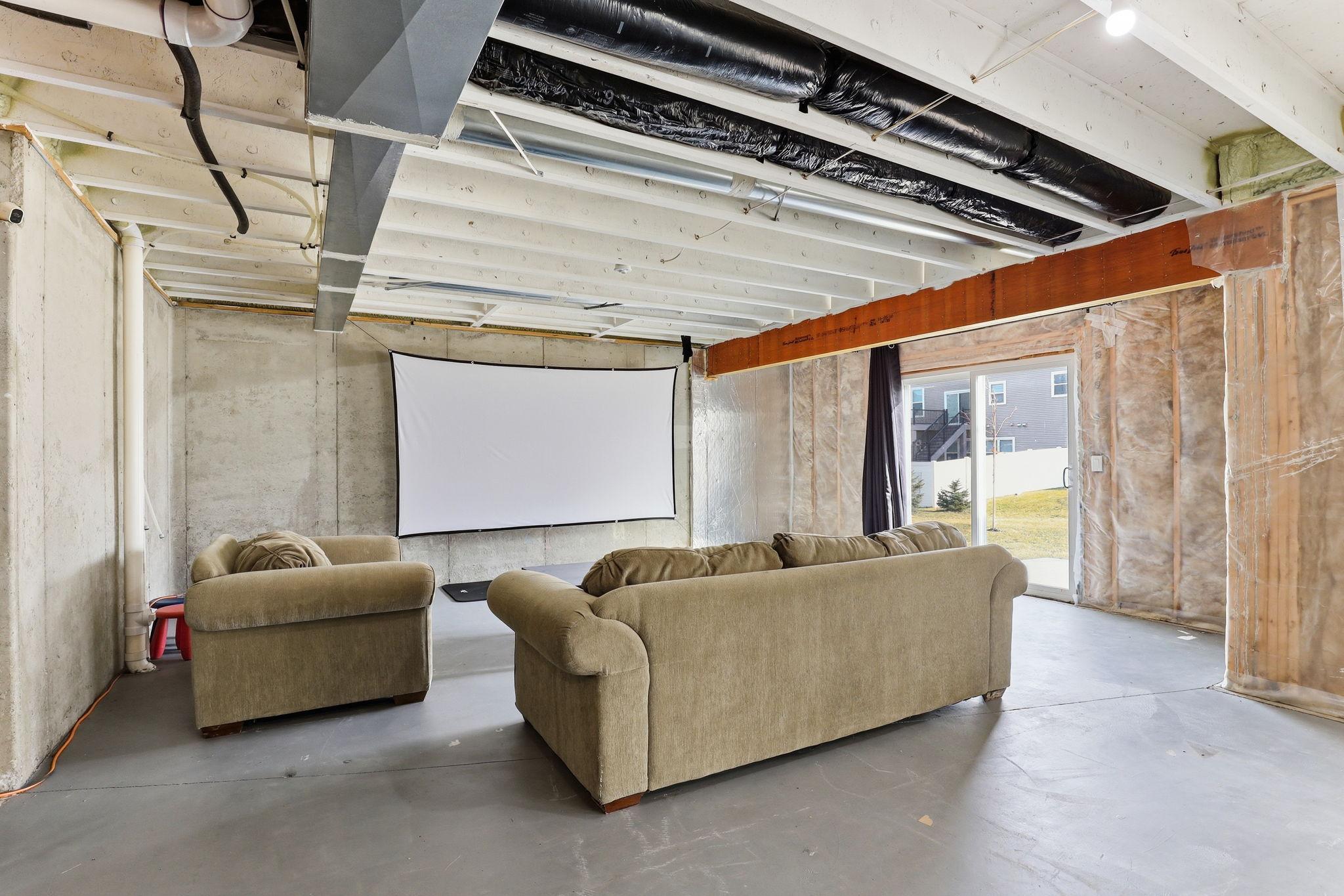 The unfinished lower level offers significant square footage, currently used as a media room with a projection screen and walkout slider to the lower patio. A blank canvas with real potential.