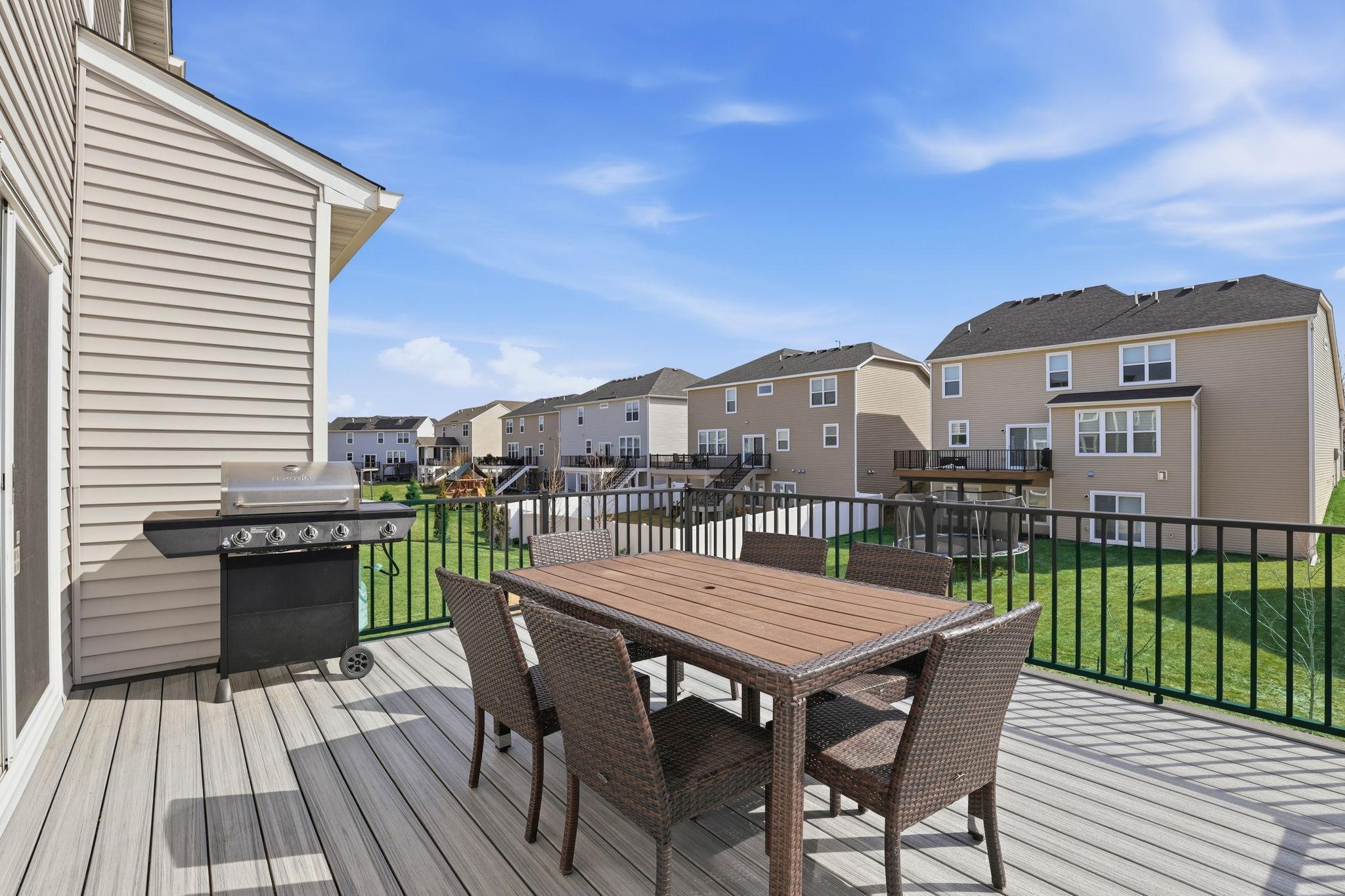 The composite deck off the main level is built for outdoor living: a dining table, a gas grill, and a black metal railing frame an open backyard view under wide Minnesota skies.