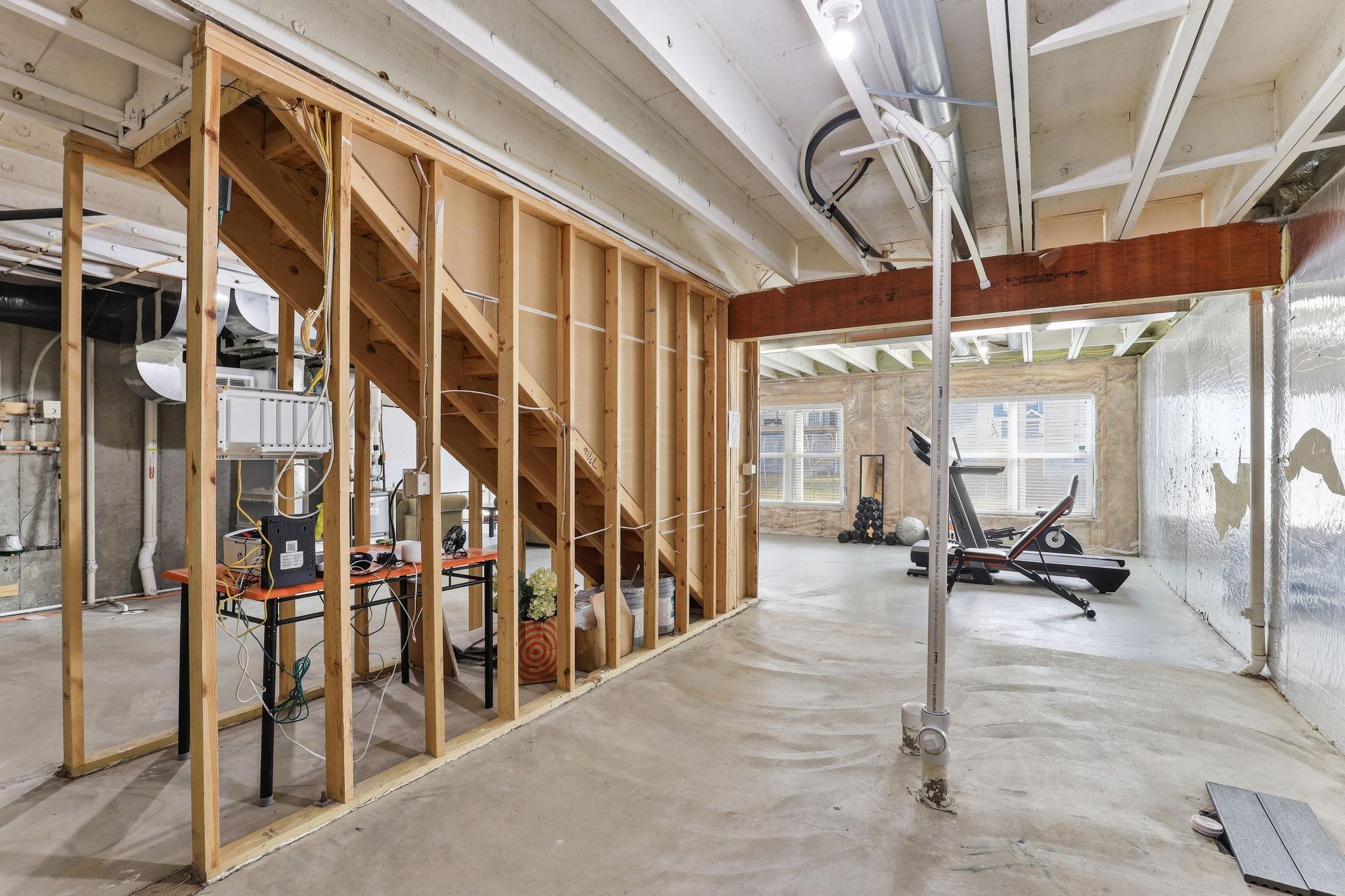 Open framing in the lower level reveals the full potential of this space. The staircase, utility rough-ins, and poured concrete walls are all in place, ready for a buyer's finish vision.