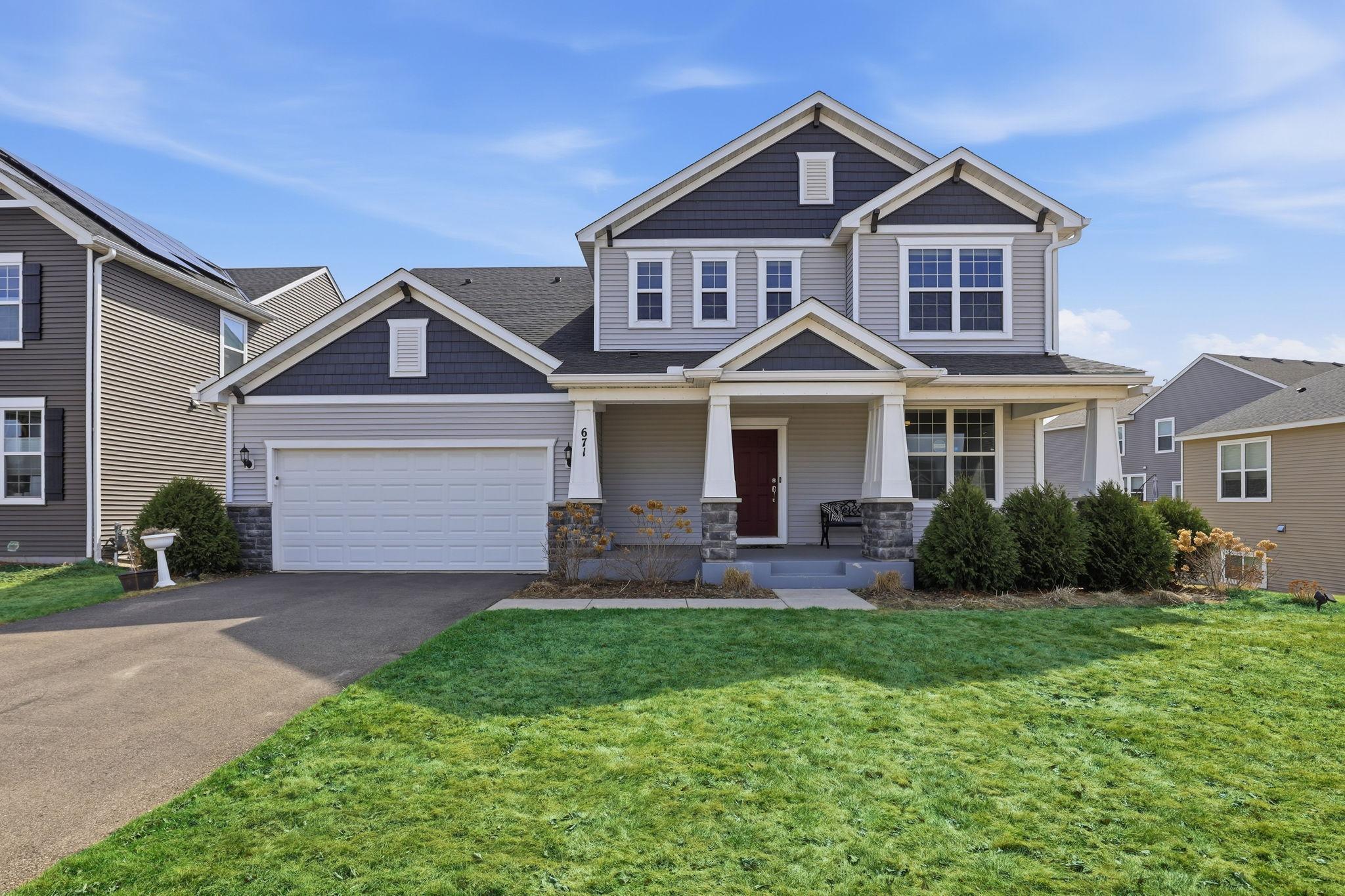 Impeccable craftsman curb appeal anchored by stacked stone columns, a white-columned front porch, and charcoal-and-gray siding. A welcoming red door and manicured lawn make an unforgettable first impression.