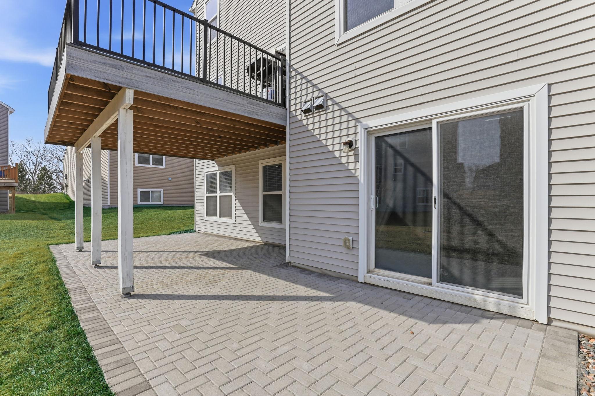 Below the deck, a herringbone-patterned patio of pavers provides a shaded outdoor retreat with walk-out access to the lower level. Two distinct outdoor living areas, two seasons of effortless entertaining.