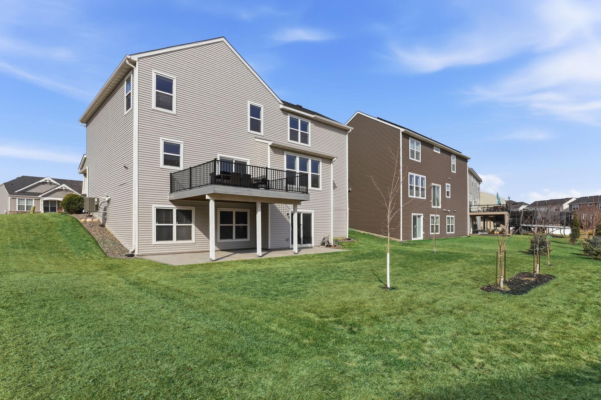 The rear elevation reveals this home's generous two-story footprint, elevated composite deck, and covered lower patio. Professionally maintained landscaping and a bright green lawn complete the picture.