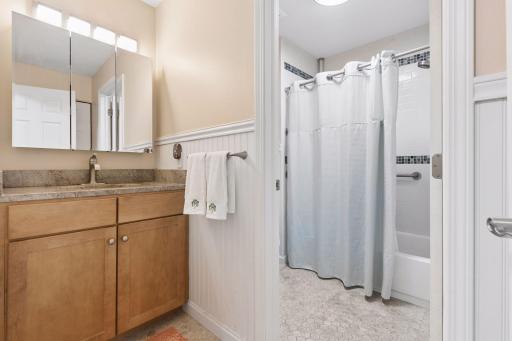 Full bathroom featuring a spacious vanity with storage, linen closet to the right, and a tub/shower combination with tile surround. Door separating the sink from the rest of the bathroom.