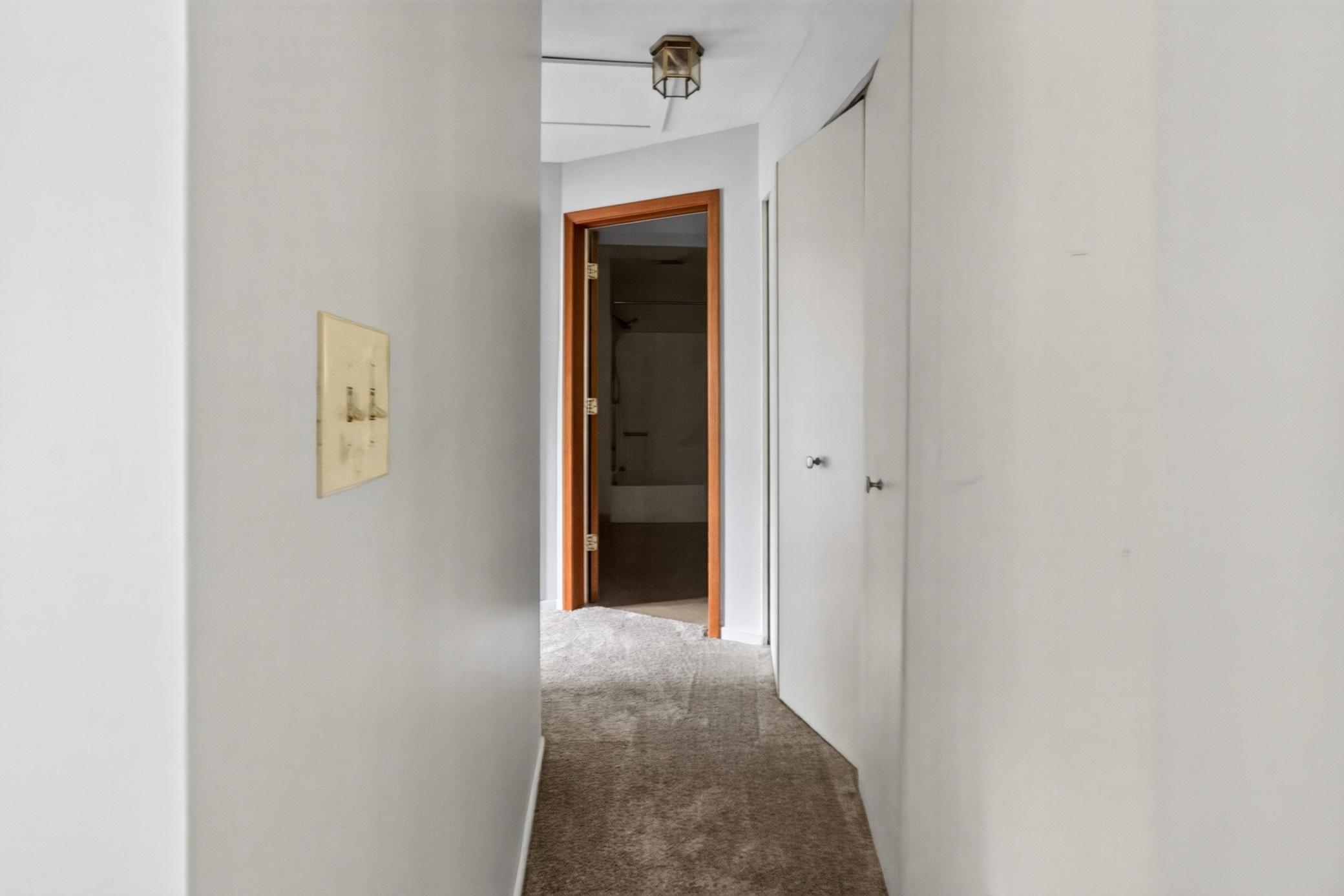 A neutral, carpeted hallway with a handy double-door closet connects the main living spaces to the private bedrooms and bath.