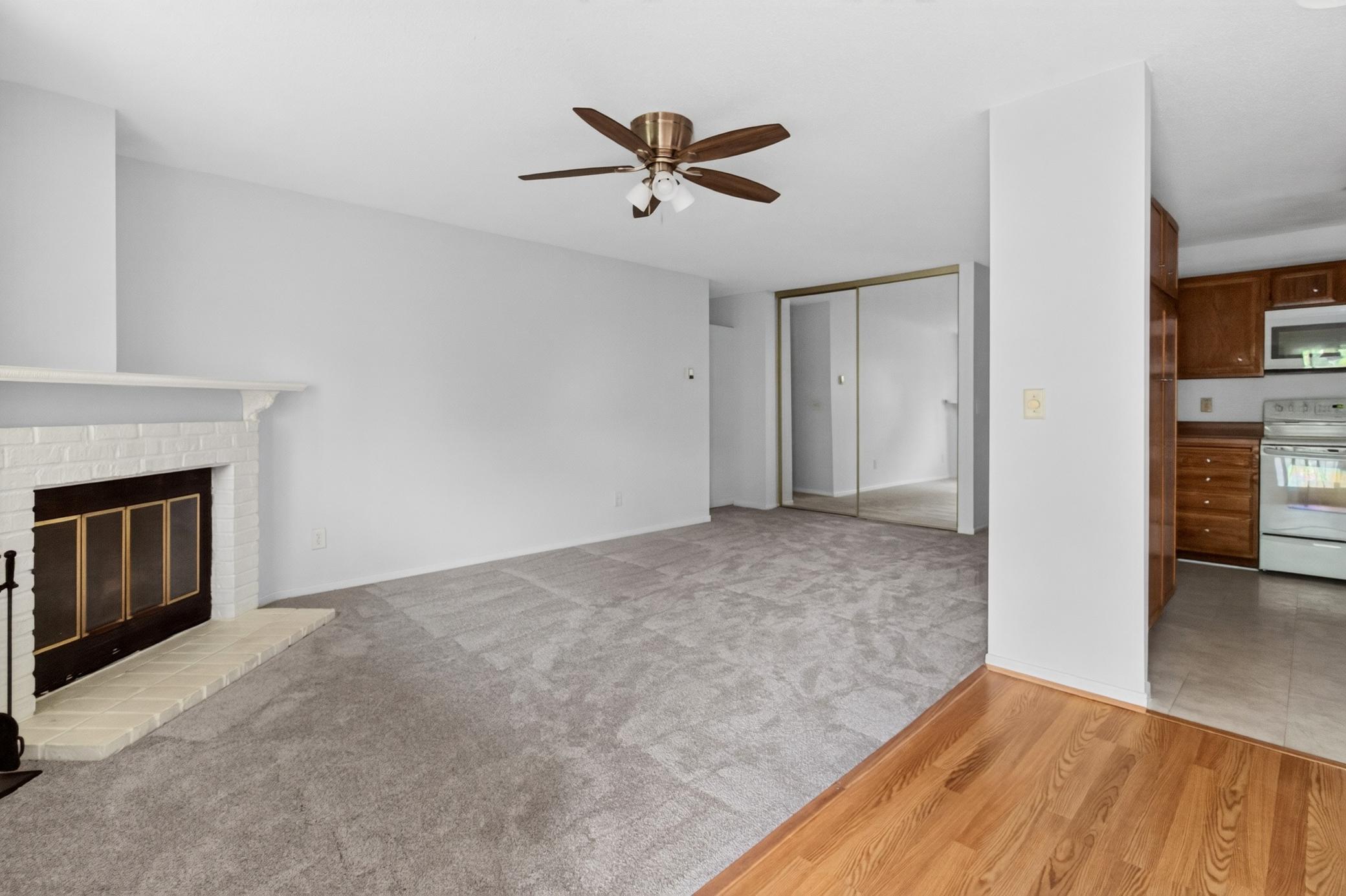 Relax in the spacious living room centered around a classic brick-faced fireplace with a mantel, complete with a ceiling fan and mirrored sliding closet doors that enhance the sense of space.