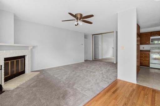 Relax in the spacious living room centered around a classic brick-faced fireplace with a mantel, complete with a ceiling fan and mirrored sliding closet doors that enhance the sense of space.