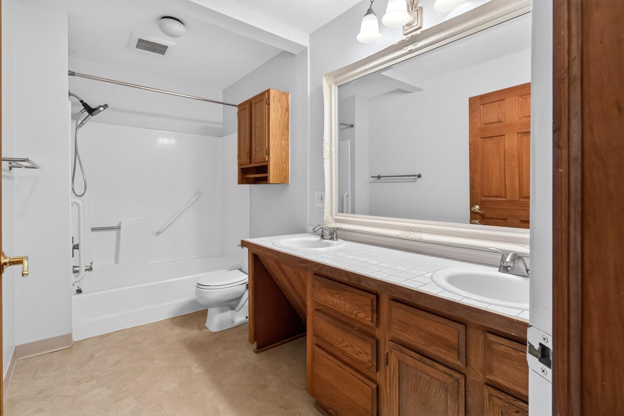 Large bathroom features an expansive double vanity with plenty of storage, an oversized framed mirror, and a clean tub/shower combo with built-in grab bars.